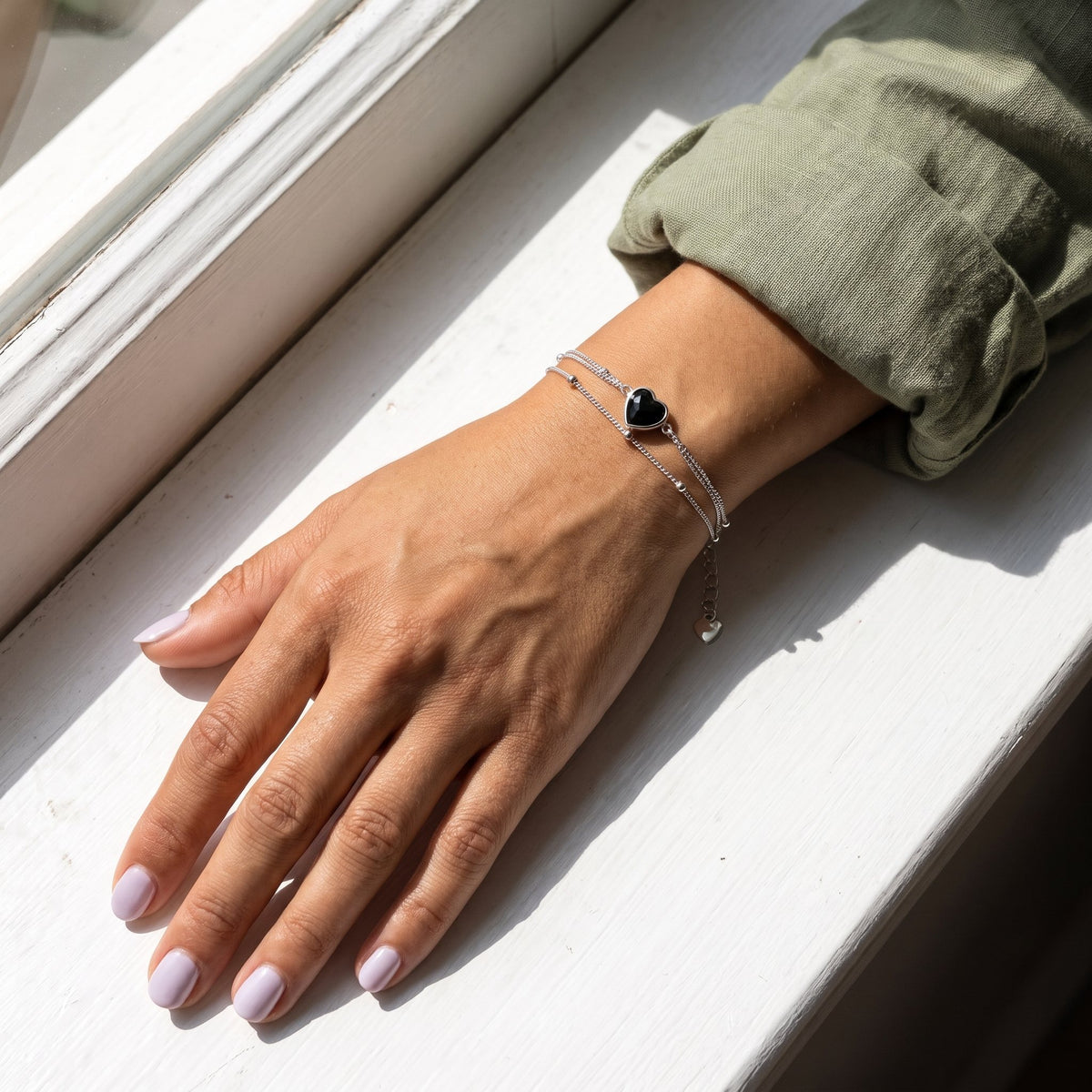 Hand wearing a black obsidian heart bracelet by a window